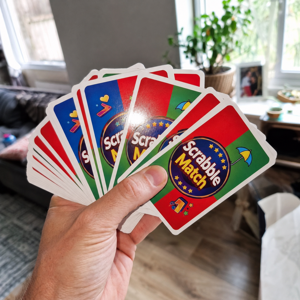 Hand holding a fan of colorful Scrabble Match cards in a living room